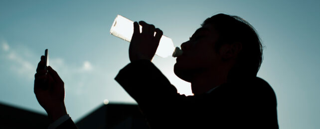 一名男子边看手机边从瓶子里喝水。